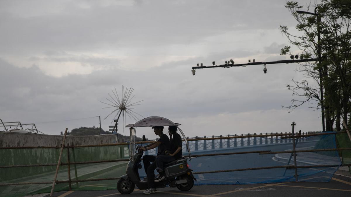 Dos personas circulan en un ciclomotor eléctrico junto a una carretera cortada ante la llegada del tifón Saudel a Yuhuan, en la provincia de Zhejiang (China).