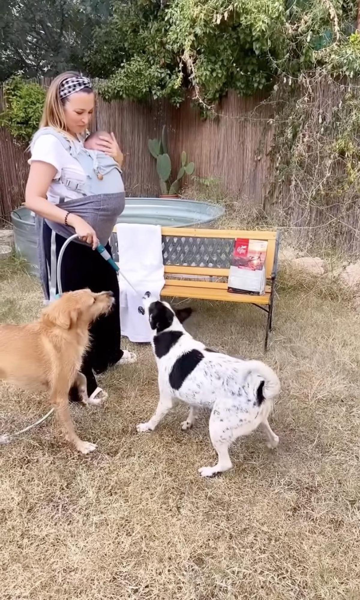 Gisela, mientras lleva al pequeño Indiana colgado en el pecho, jugando con sus perros Peter y Lilu