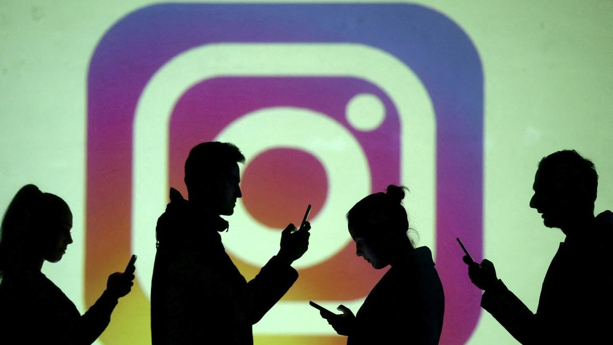 Personas consultando sus teléfonos móviles pasan por delante de una pantalla en la que sale proyectado el logo de Instagram