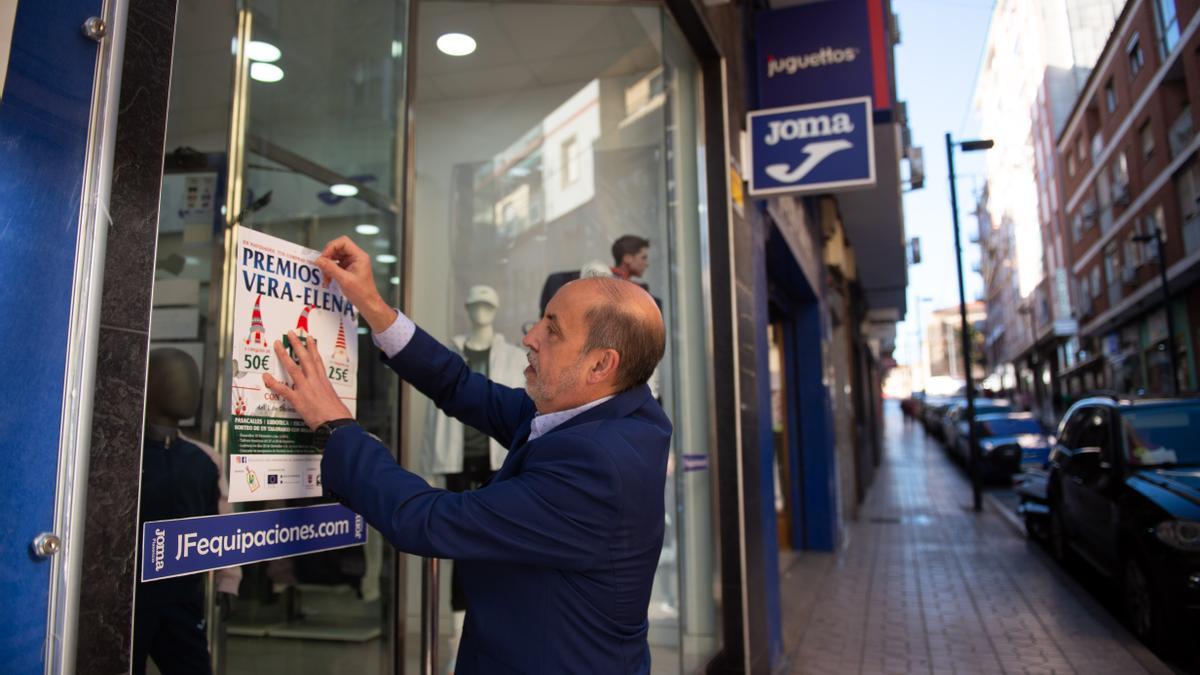 El presidente del comercio de Vera-Elena en Plasencia coloca un cartel de la campaña.