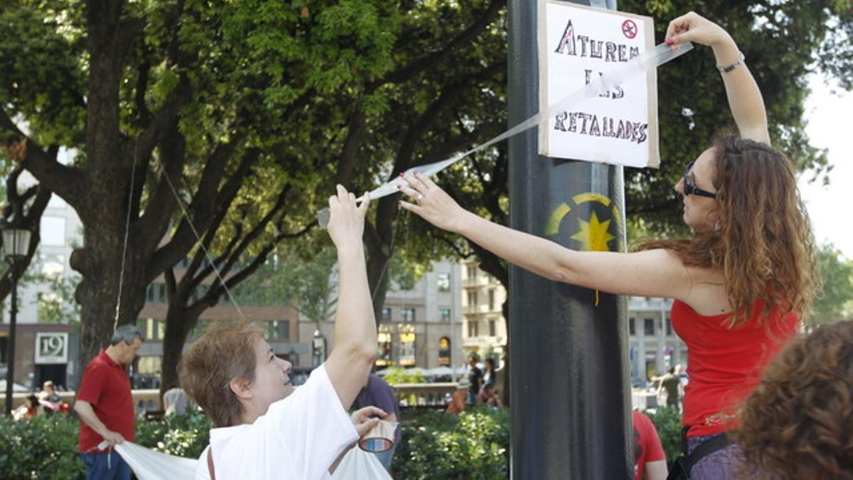 Dos mujeres cuelgan una pancarta contra los recortes.