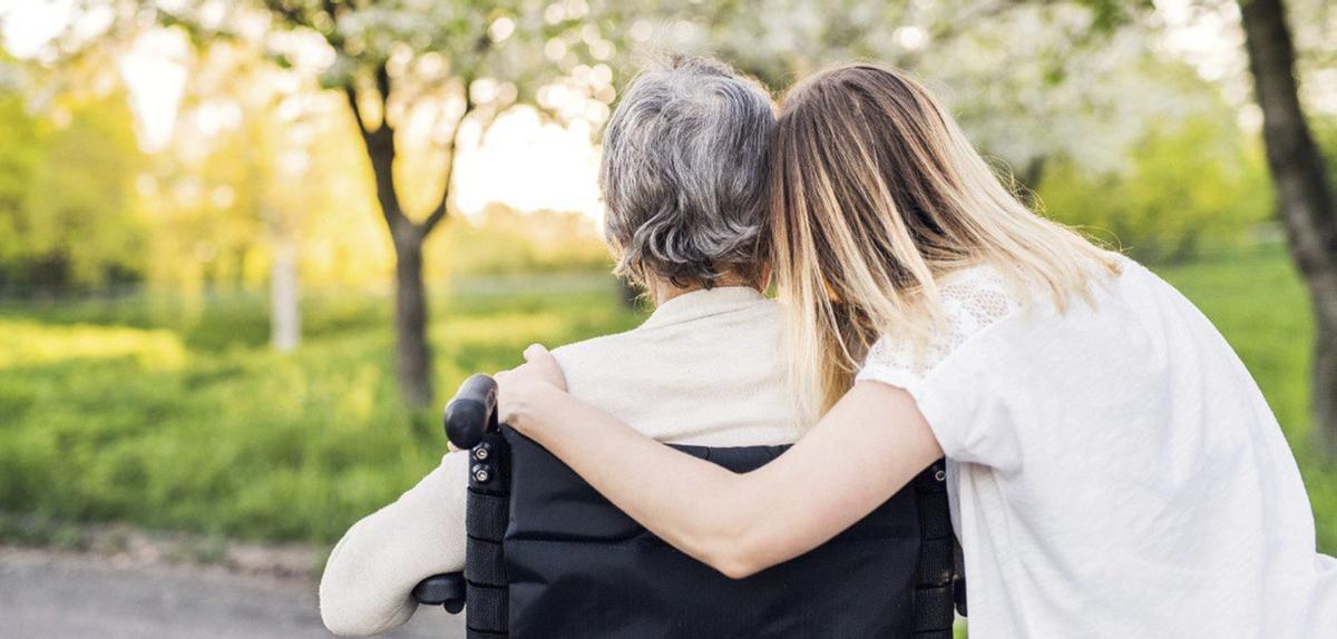 Una cuidadora con una persona mayor en silla de ruedas.