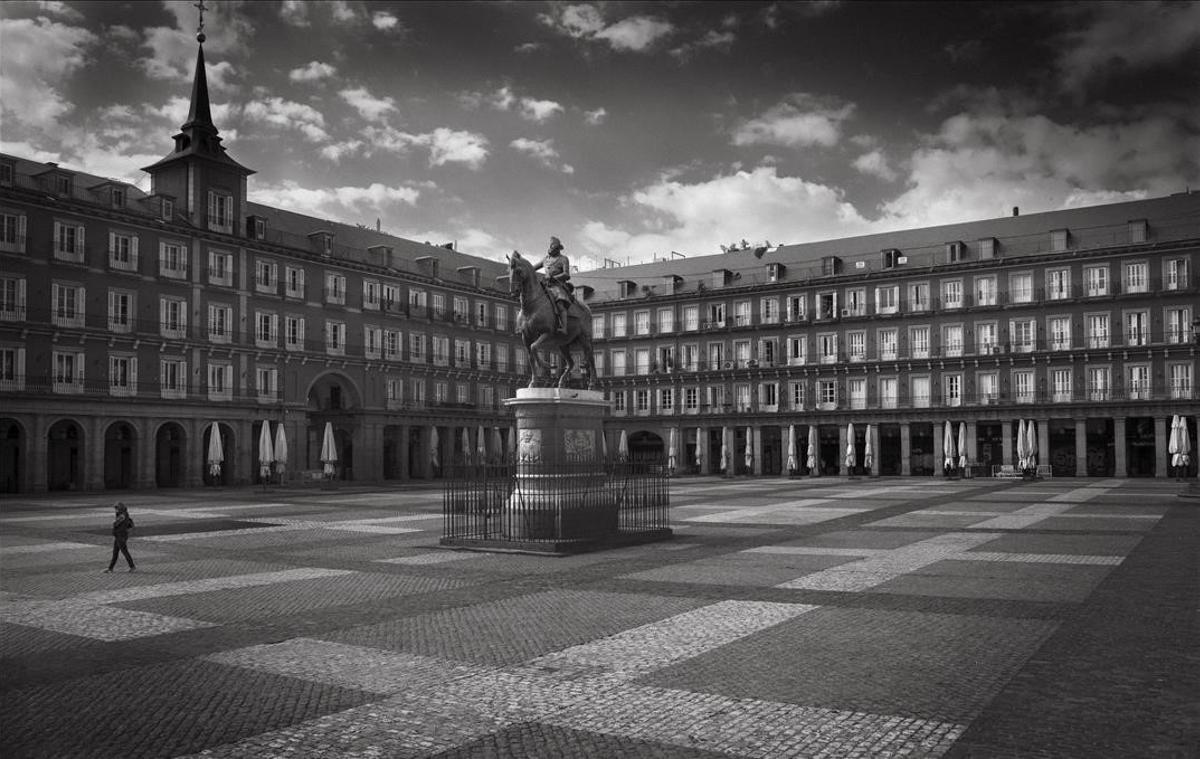 Una persona cruza la solitaria Plaza Mayor de Madrid el primer día del confinamiento. Las sombrillas recogidas son el único recuerdo de las bulliciosas terrazas.