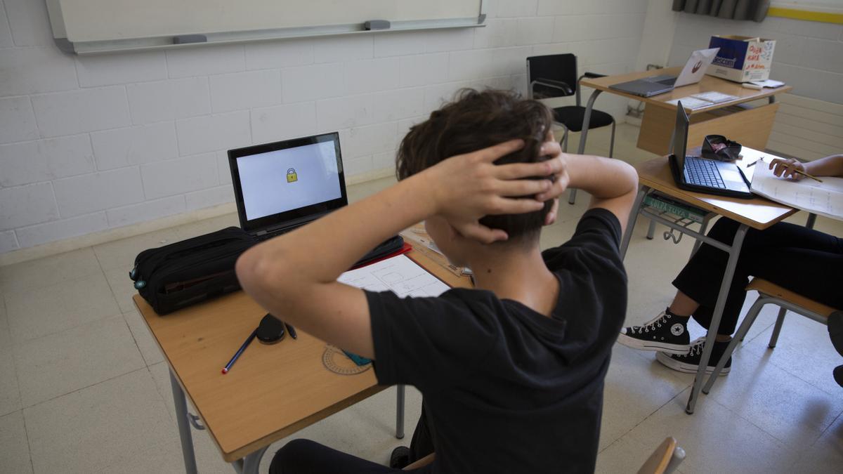 Alumno de un instituto catalán con un ordenador portátil y papeles sobre el pupitre, este curso.