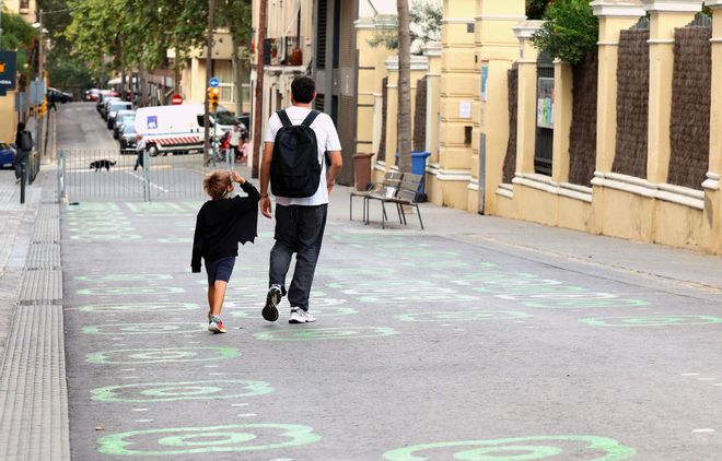 Un padre y un hijo caminan junto a un entorno escolar pacificado en Barcelona.