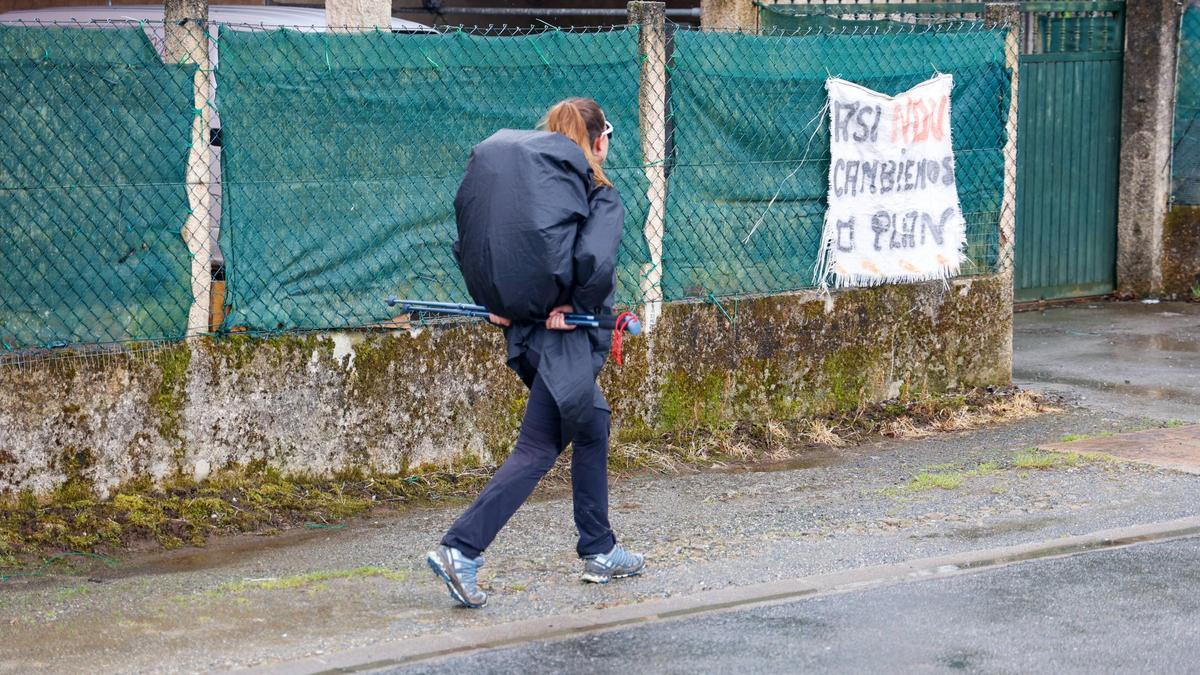 Una peregrina pasa ante un cartel contra el Plan Especial do Camiño en la zona de Lavacolla, en Santiago