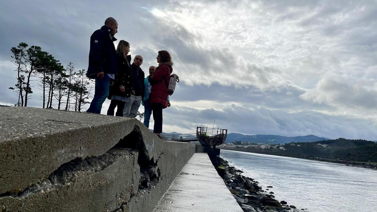 En primer plano, daños en el espigón de Navia. Al fondo, diputados y miembros del equipo de gobierno naviego durante la visita.