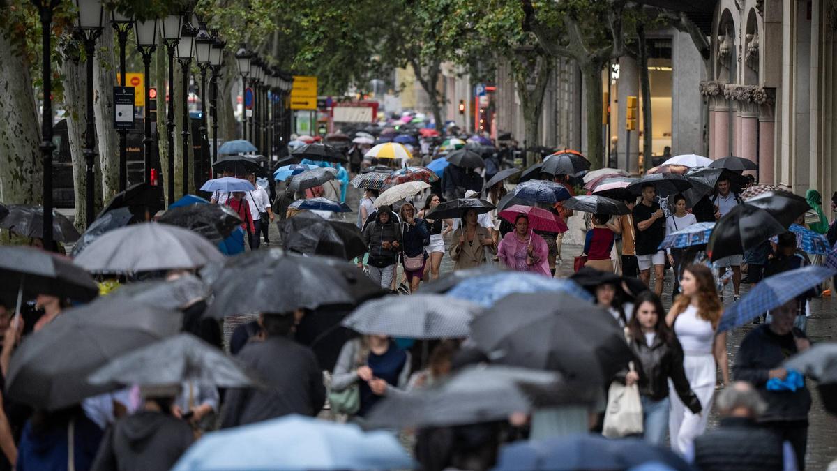 Turistas y locales se protegen de la lluvia con paraguas y chubasqueros en el centro de Barcelona.