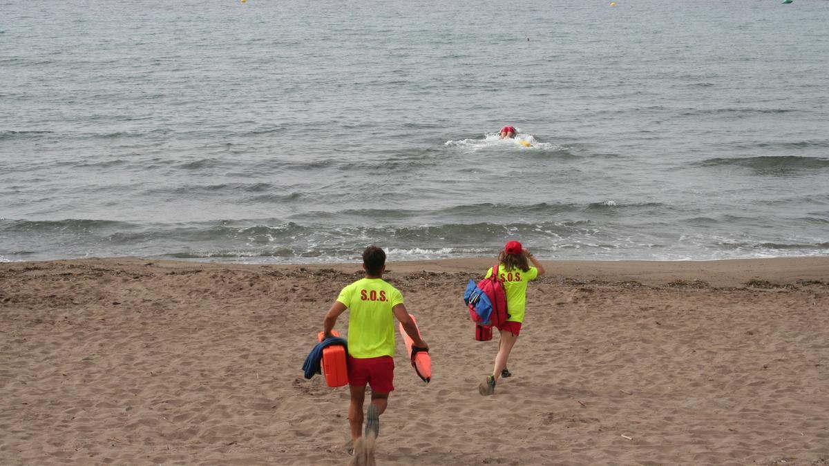 Dos socorristas corren por la arena mientras otro se tira al agua para realizar un rescate en el litoral lorquino, este lunes.