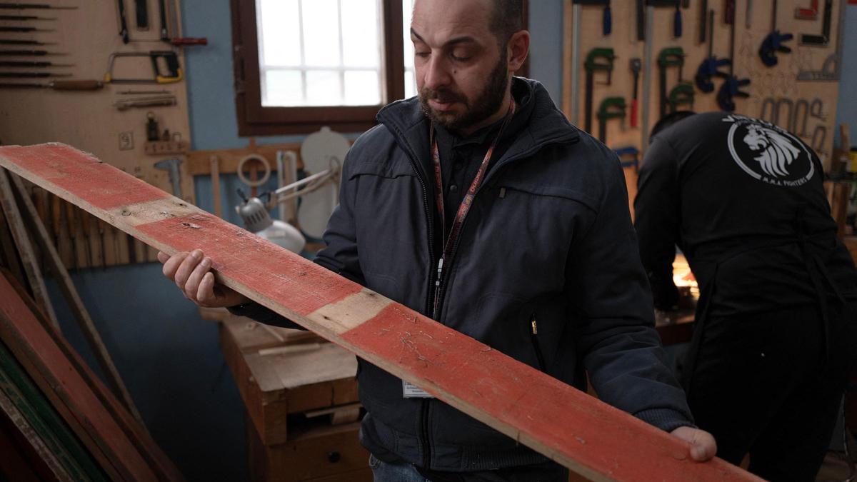 Un preso sostiene un trozo de madera procedente de una barca en la que viajaban inmigrantes llegados a Lampedusa, parte del proyecto 'Violines del mar'