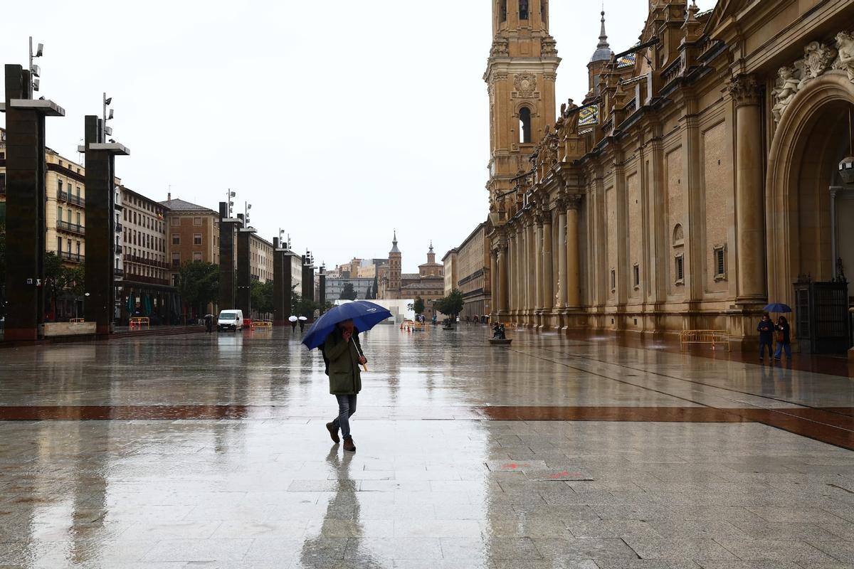 Un hombre se protege de la lluvia mientras camina por la plaza del Pilar de Zaragoza este jueves