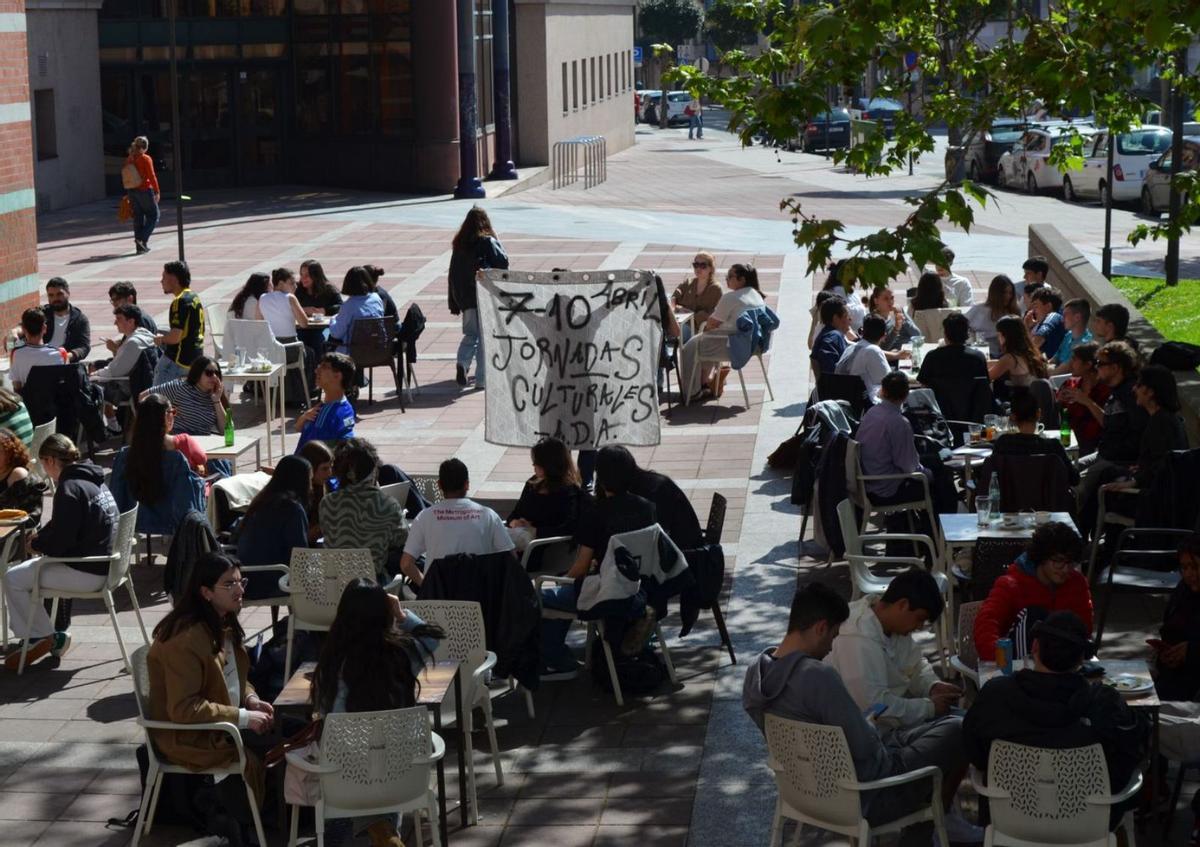 Una de las Amigas de lo Ajeno exhibe la pancarta de las jornadas culturales ante la indiferencia de la mayoría de los estudiantes en la terraza de la cafetería del campus del Milán.