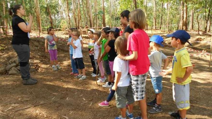 La técnica Begoña explica los fundamentos de la arqueología al grupo infantil, junto al yacimiento.  // E. G.