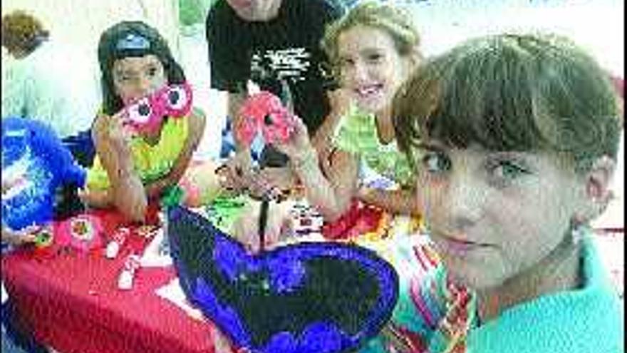 Tres niñas muestran sus caretas bajo la mirada del monitor del taller infantil.