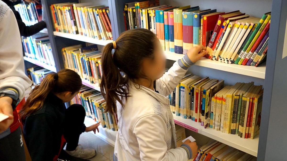 Dos niñas consultan varios libros en la biblioteca de Benetússer
