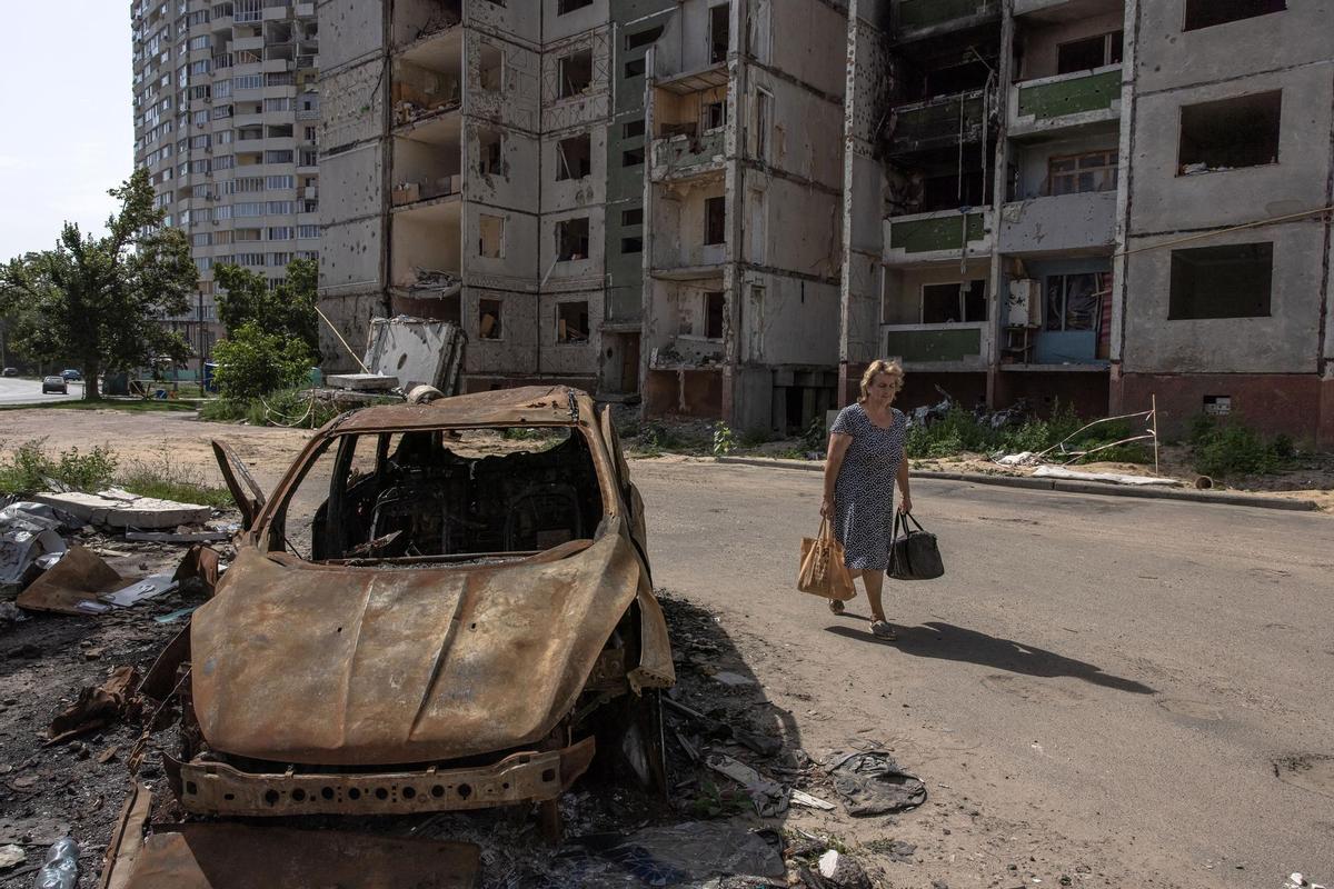 Una mujer pasa este lunes junto a un coche quemado y un edificio residencial dañado en Chernihiv, en el norte de Ucrania. EFE/EPA/ROMAN PILIPEY