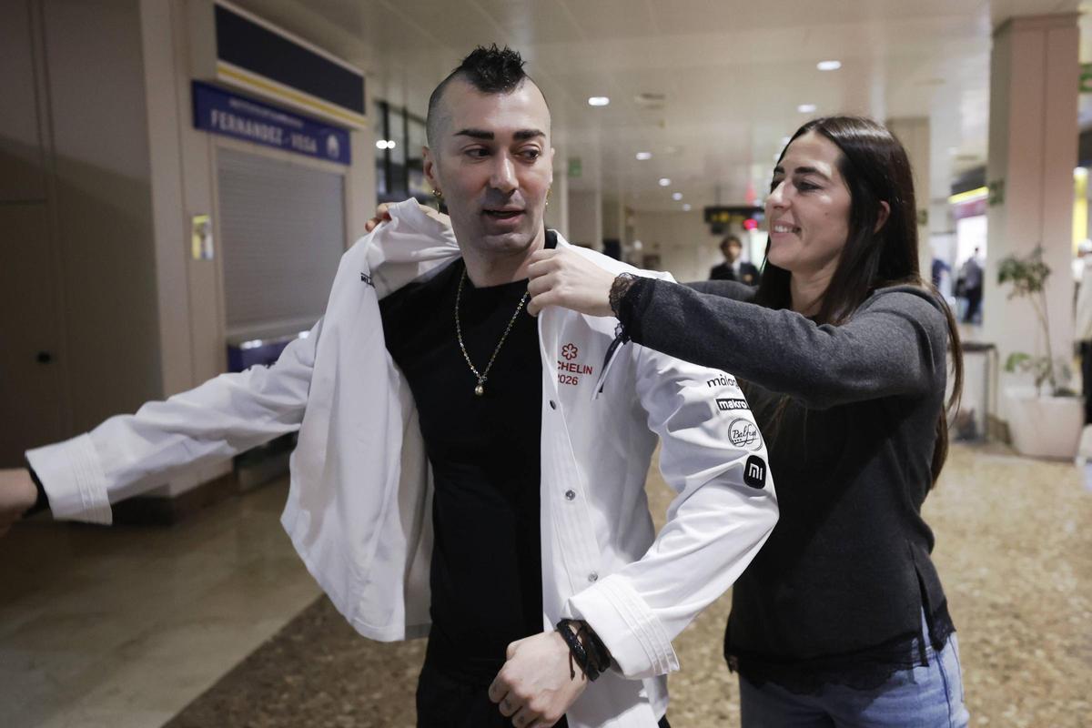 Ana Fernández pone la chaquetilla de chef Michelin a su hermano Diego, en el aeropuerto de Asturias, recién llegados de Málaga.