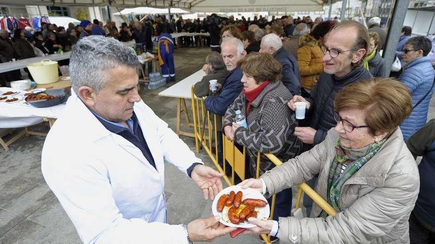 Un miembro de la organización entrega un plato con chorizos a una vecina.  // Bernabé/Javier Lalín