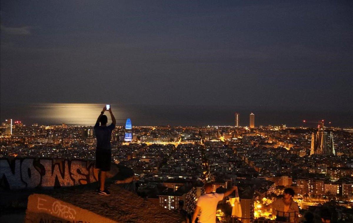  Un chico toma una foto de Barcelona, al anochecer.