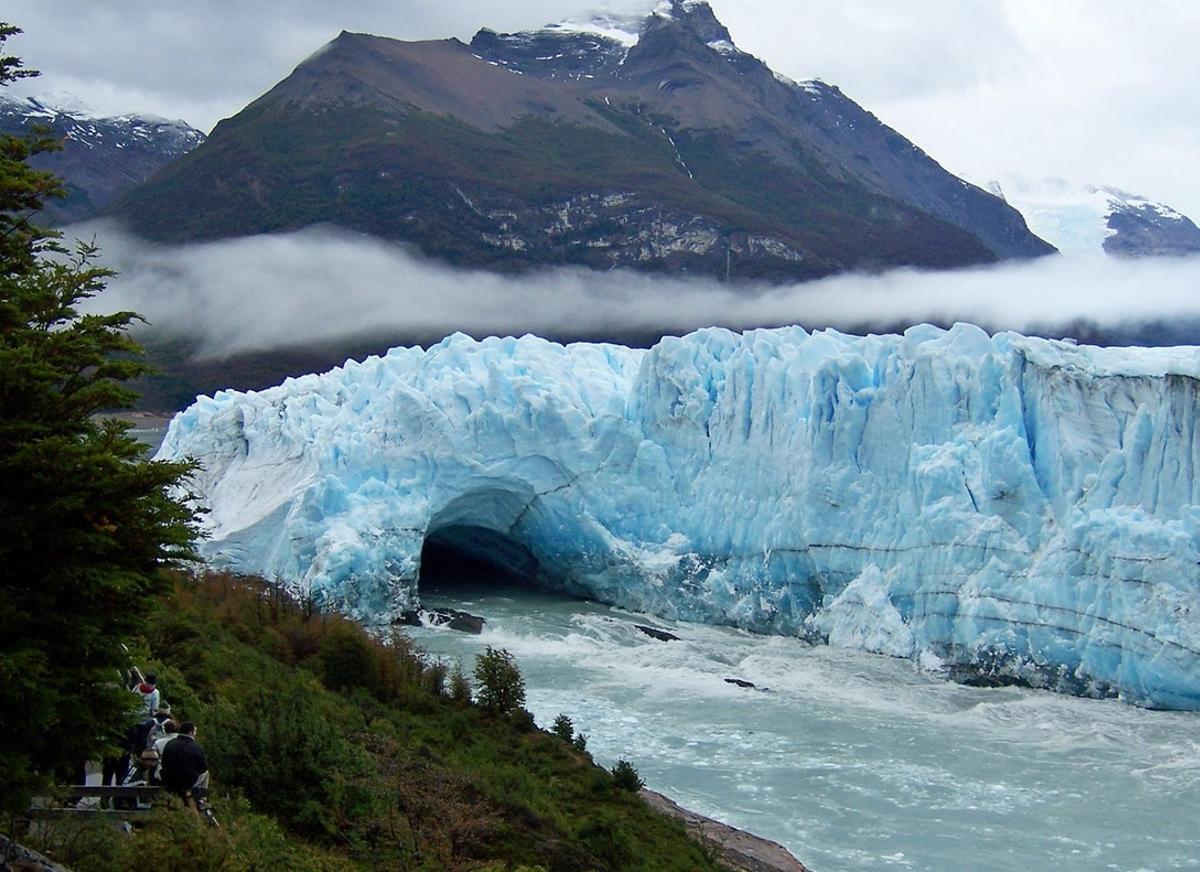 Tourists (bottom L) watch for the long-awaited rupture of the leading edge of the Perito Moreno glacier as the waters of Lake Argentino open a tunnel in the glacier, widening it until its collapse in a massive explosion of ice fragments and water, near the city of El Calafate in the Patagonian privince of Santa Cruz, southern Argentina, March 12, 2006. The Perito Moreno glacier, part of the Los Glaciares National Park, a World Heritage site, is unusual in that it is still growing forward at the accelerated rate of between 30 and 60 cm per day.  NO SALES   NO ARCHIVES   Photo taken March 12, 2006.  REUTERS/CoTeCal and Parque Nacional Los Glaciares/Handout