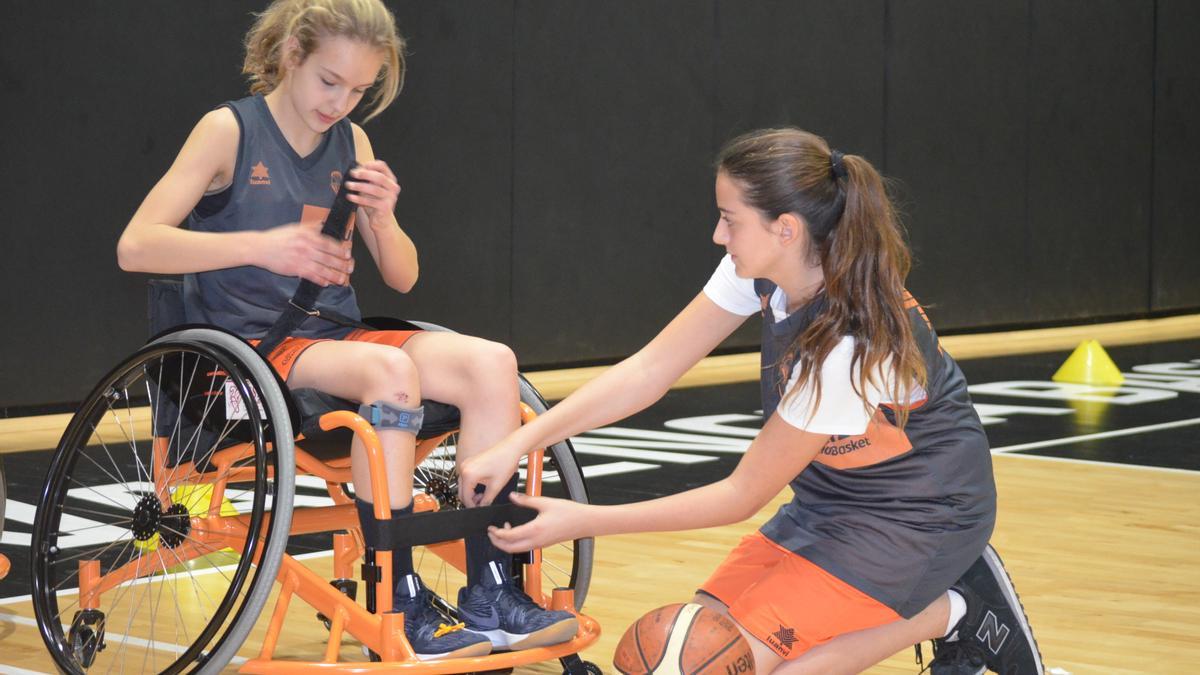 Una jugadora de baloncesto en silla de ruedas junto a una monitora en un entrenamiento.