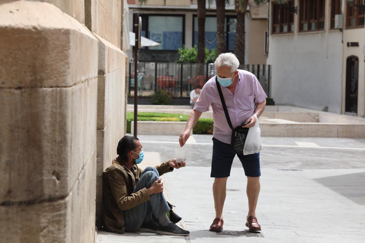 Un ciudadano entrega unas monedas a un mendigo junto a la basílica de Santa María, en Elche