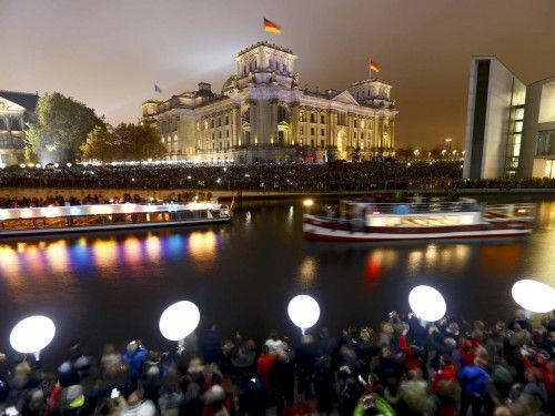 People stand outside the Reichstag lower house of parliament builiding under lit balloons, which are part of the installation 'Lichtgrenze' (Border of Light) in Berlin