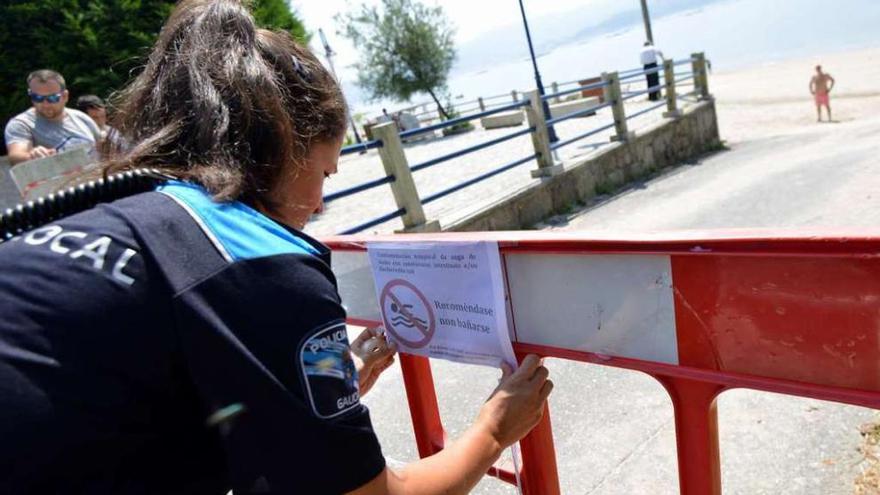 Una agente de la Policía Local coloca un cartel que desaconseja el baño.