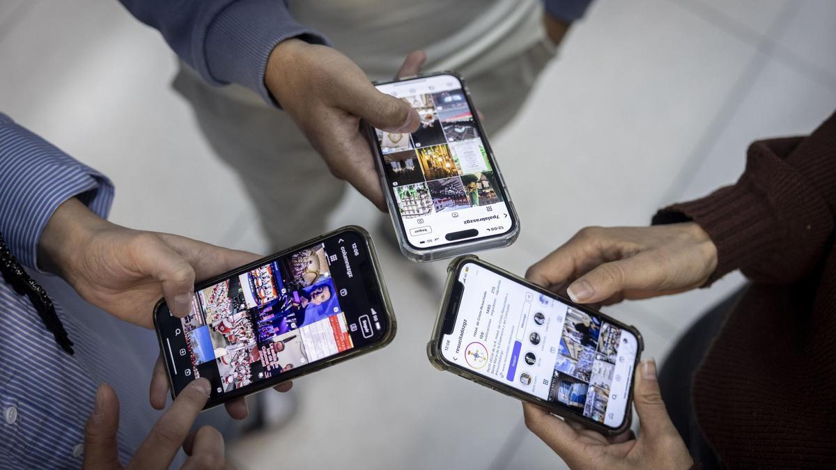 Varias personas consultan en sus móviles información de cofradías en redes sociales.