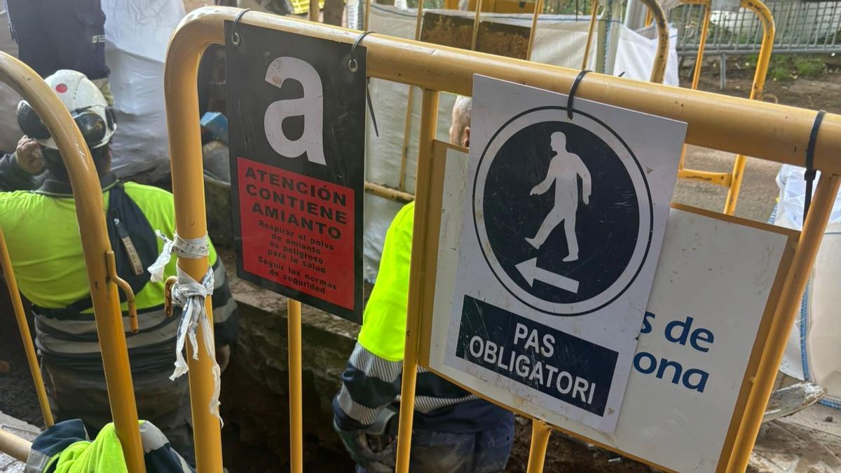 Un cartel de advertencia de la presencia de amianto y del peligro de respirar sus fibras en la zanja donde los operarios reparan la presunta avería que ha provocado el corte de agua en calles de Sant Martí.