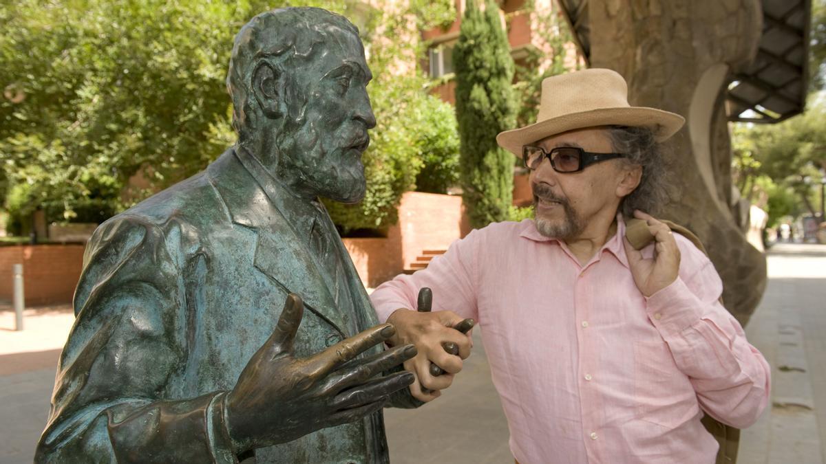   Lluis Llongueras se da la mano con el Gaudi de bronce de Joaquim Camps, frente al Portal Miralles en agosto de 2011