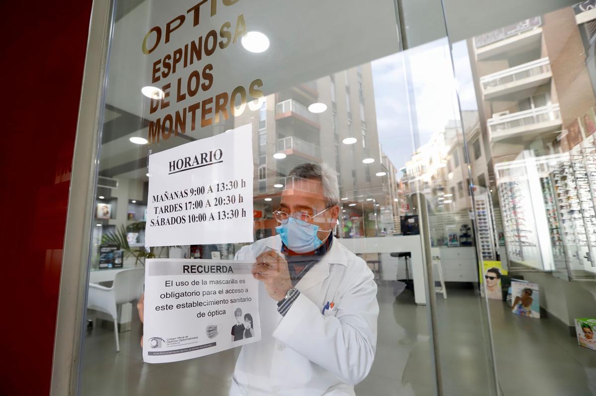 El empleado de una óptica retira el cartel donde se avisaba de la obligatoriedad de usar mascarilla en estos establecimientos.