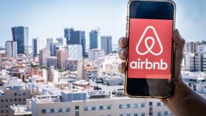 Un teléfono con logo de la empresa AirBnb, con el skyline de LHospitalet de Llobregat de fondo