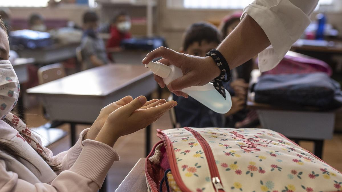 Una profesora administra gel desinfectante a una alumna en un aula.