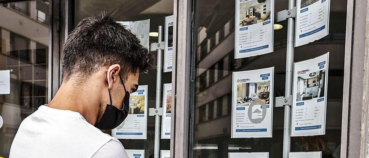 Un joven mira el escaparate de una inmobiliaria.