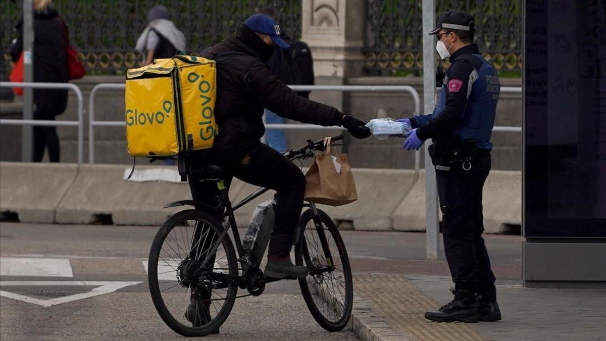 Un policía entrega una mascarilla a un repartidor de Glovo
