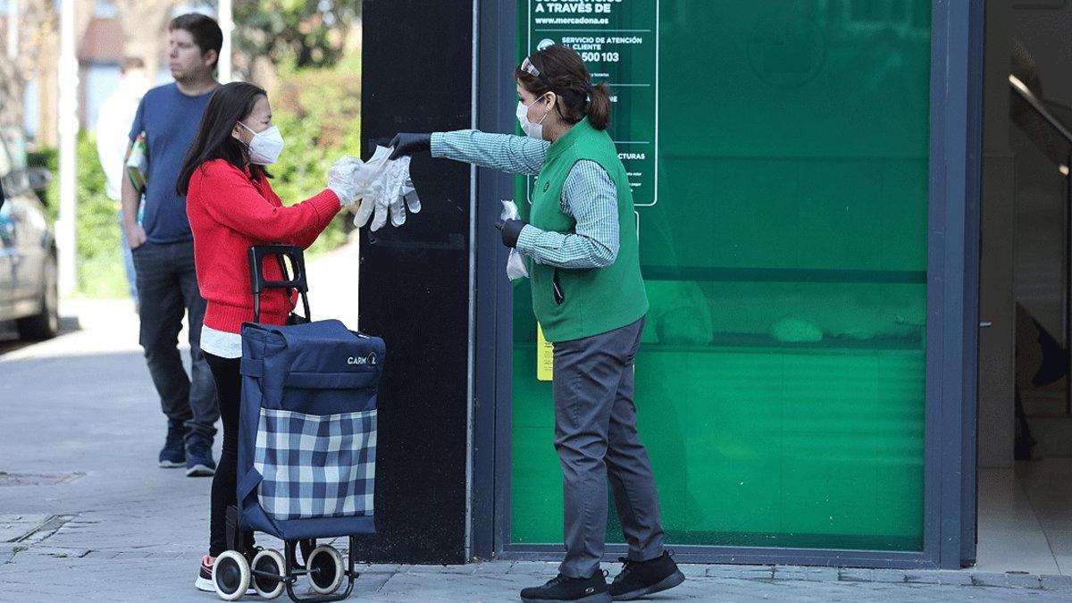 Una trabajadora de un supermercado entrega un par de guantes a una clienta, en Madrid, el pasado 8 de abril
