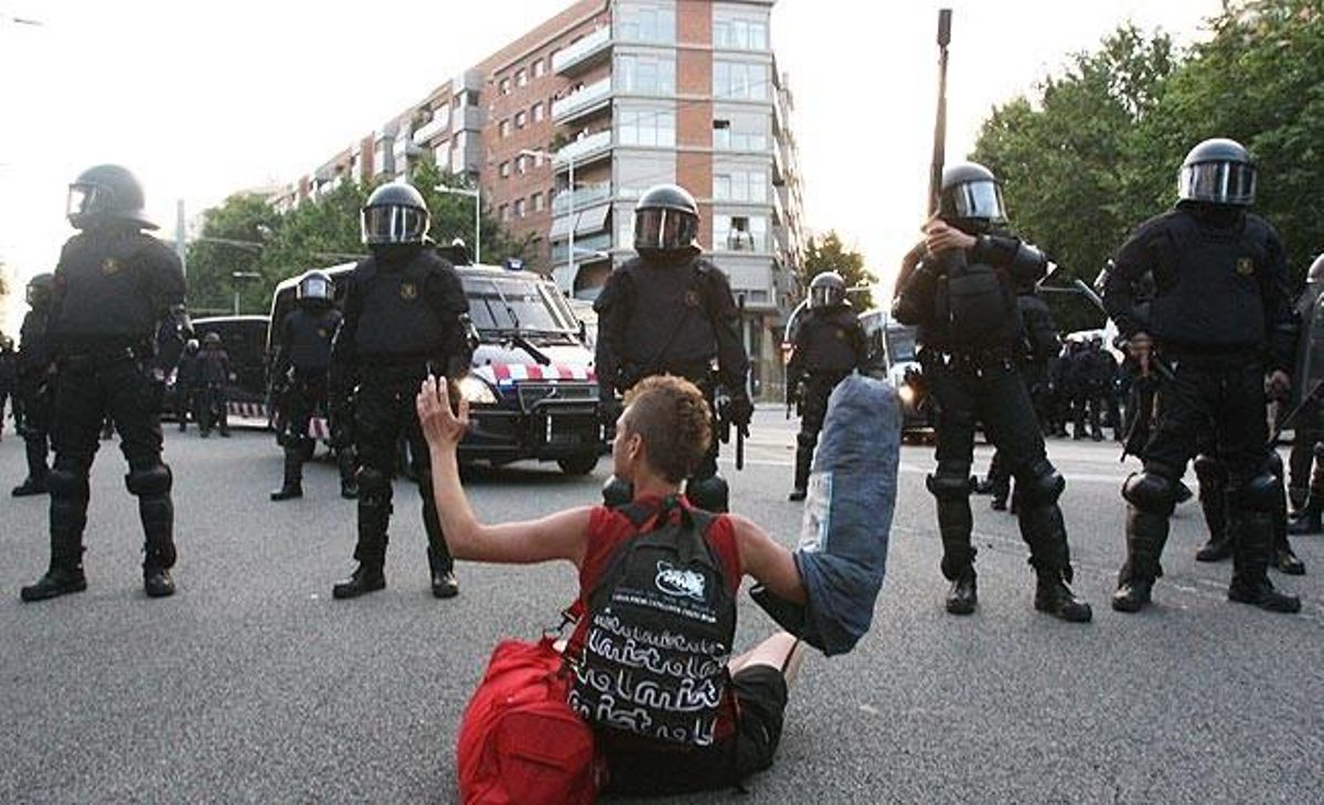 Un jove es manté assegut davant diversos agents antiavalots dels Mossos d’Esquadra.