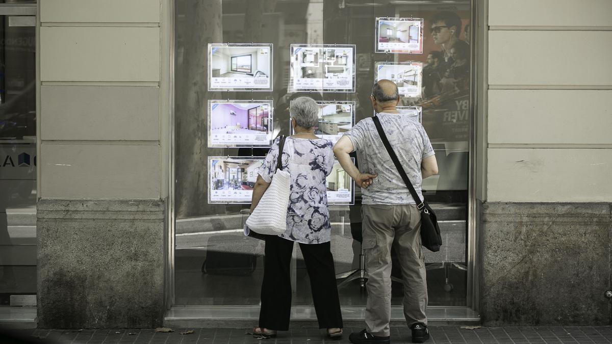 Una pareja escruta el precio de pisos en una agencia inmobiliaria de Barcelona.
