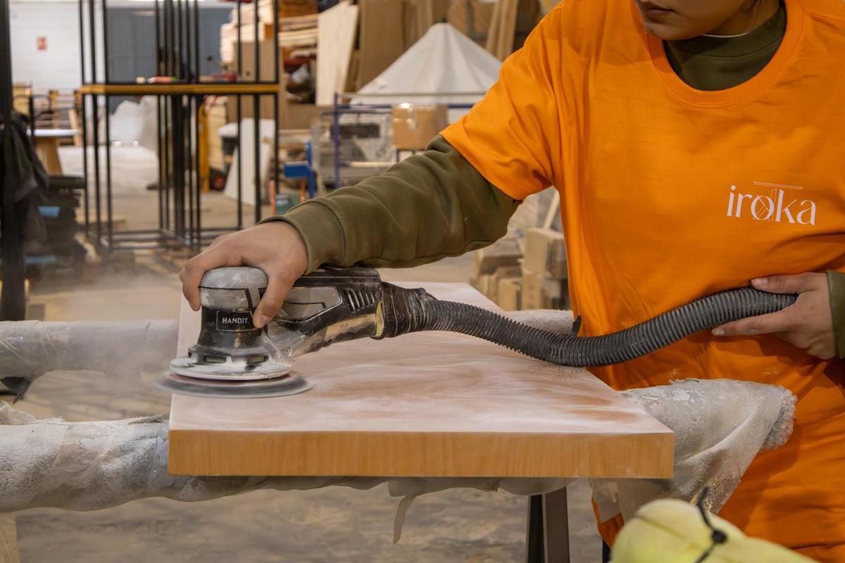 Una trabajadora de Bois Maisson manejando una lijadora sobre una pieza de madera de haya en el taller de esta empresa del municipio sevillano de Carmona.