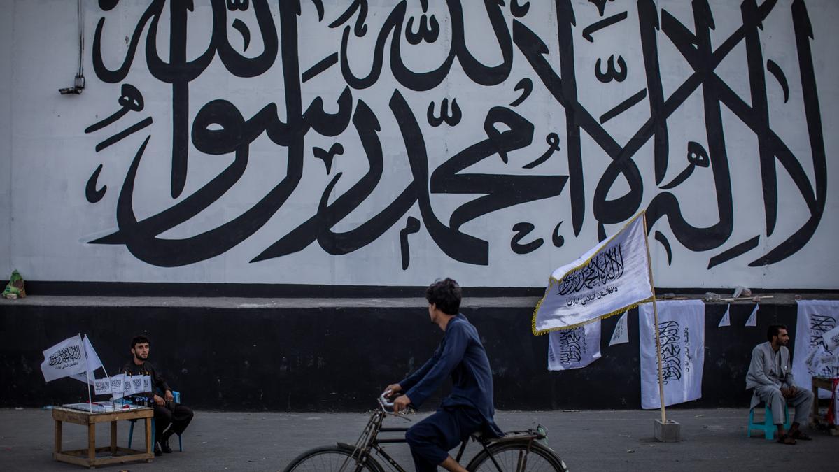 Un hombre vende banderas de los talibán frente al muro de la antigua Embajada de EEUU en la capital de Afganistán, Kabul, ahora cubierta con un mural religioso.