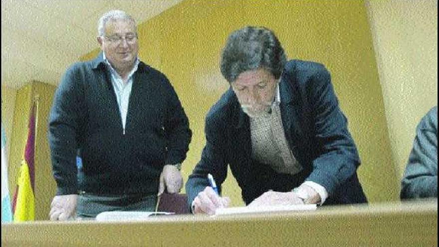 Sergio Villanueva firma el acta de la asamblea de la Atlética Avilesina durante su proclamación como presidente, con su antecesor, Juan Garrudo, a la expectativa.