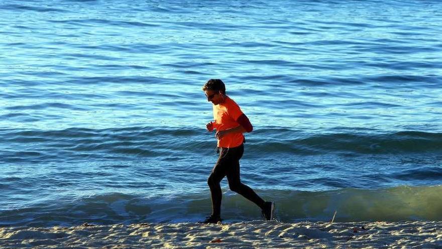 Un hombre corre por la playa de Samil con los auriculares conectados a su teléfono móvil. // Marta G. Brea