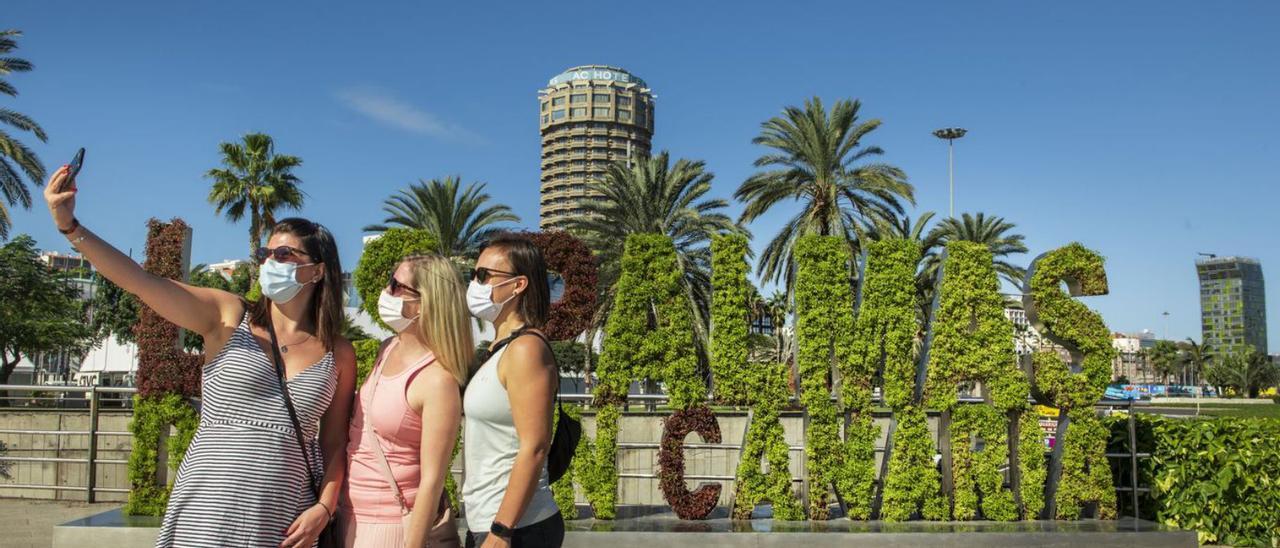 Tres turistas se hacen una foto en la plaza de Canarias, junto a un cartel vegetal alusivo a la ciudad. | | TURISMO LPA / NACHO GONZÁLEZ