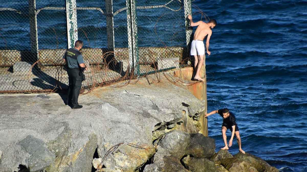 Dos inmigrantes cruzan la frontera entre Marruecos y España, en Ceuta, en presencia de un Guardia Civil.