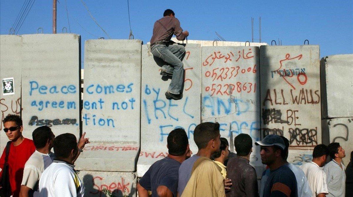 Un palestino trepa por un bloque de cemento mientras otros caminan junto a la barrera israelí que separa la población cisjordana de Abu Dis, en las afueras de Jerusalén, el 19 de julio del 2004.