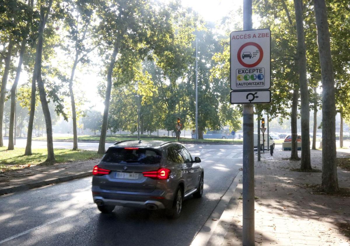 Un cartell que indica l’accés al perímetre de la ZBE de Girona des de la Devesa, amb un vehicle circulant al costat. | XAVIER PI/ACN