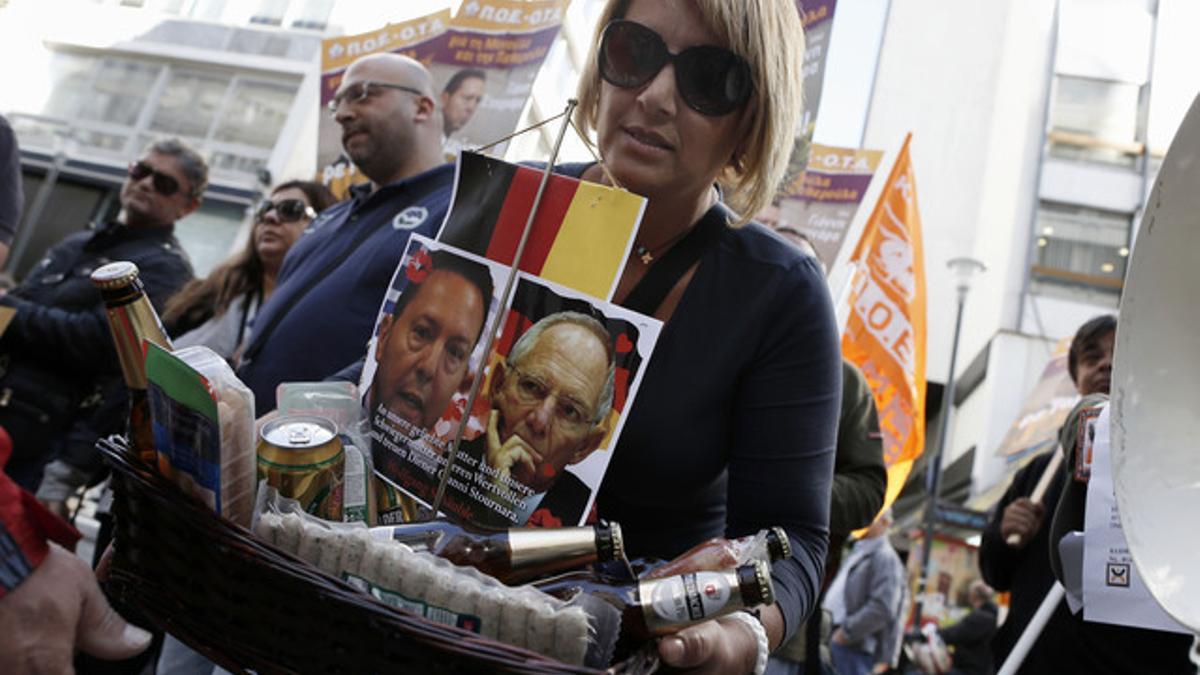 Una mujer lleva una cesta con comida y las fotos de los ministros de Finanzas griego (izquierda) y alemán, este jueves.