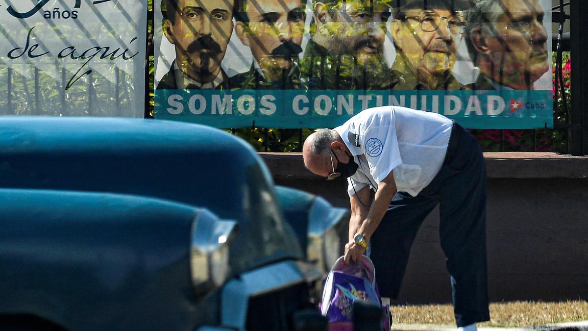 Un hombre con su coche frente al cartel del Partido Comunista cubano.