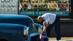 Un hombre con su coche frente al cartel del Partido Comunista cubano. 